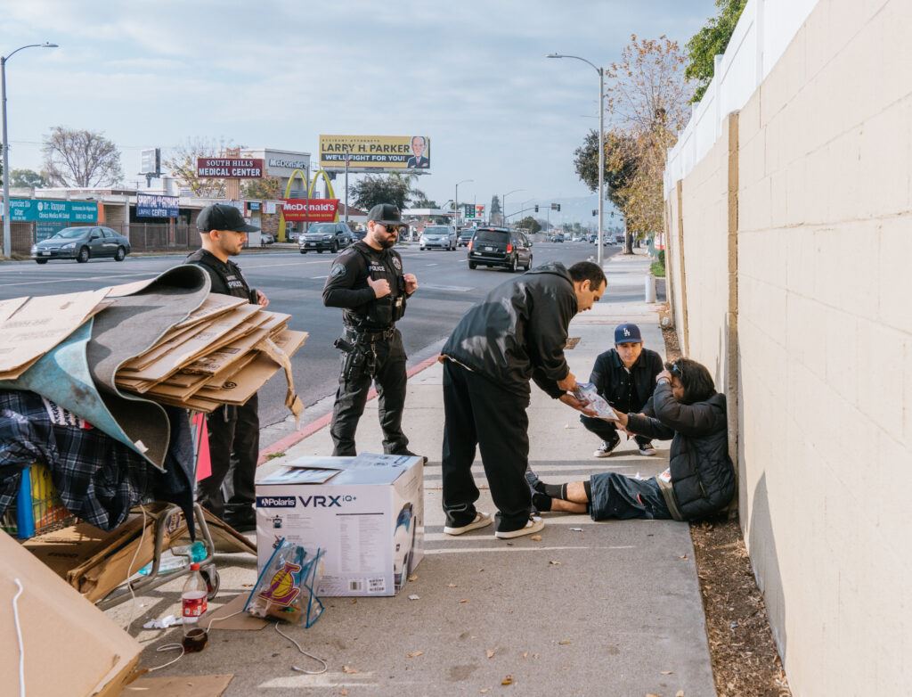 Person Helping the Homeless as Police Supervise